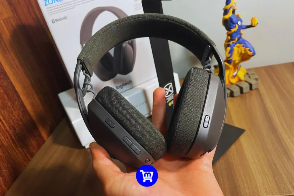 Logitech Zone Vibe 100 é bom? Análise Completa em 2025 4 Headset Logitech Zone Vibe 100 na cor preta sendo segurado, mostrando as almofadas em tecido e design over-ear com acabamento em plástico cinza.