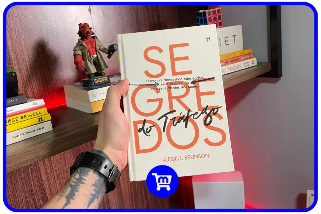 Trilogia Segredos H1 Editora: O Guia para Empreendedores em 2025 11 Livro Segredos do Tráfego de Russell Brunson em edição da H1 Editora sendo segurado em frente a uma estante.