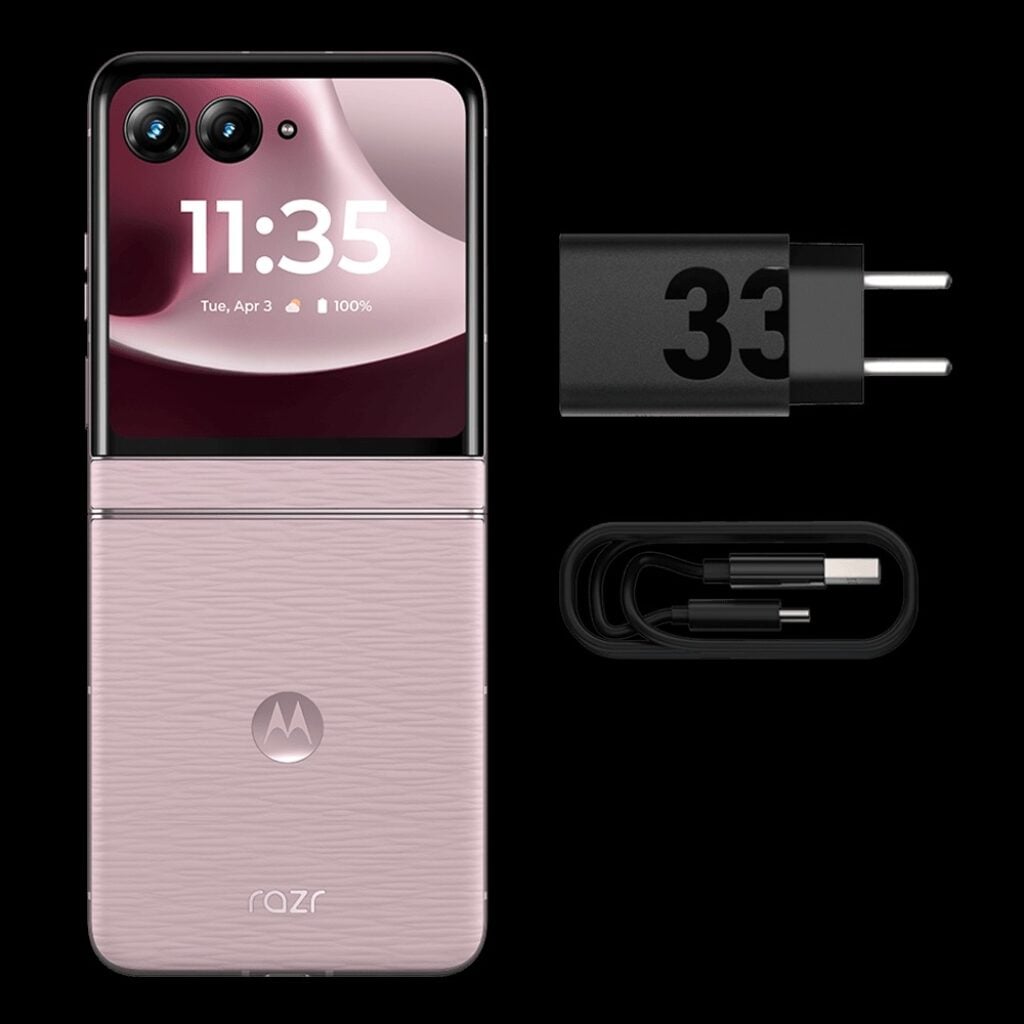 Smartphone Motorola Razr 70 rosa fechado exibindo 100% de bateria na tela externa, ao lado de um carregador de tomada preto com o número "33" e um cabo USB-C.
