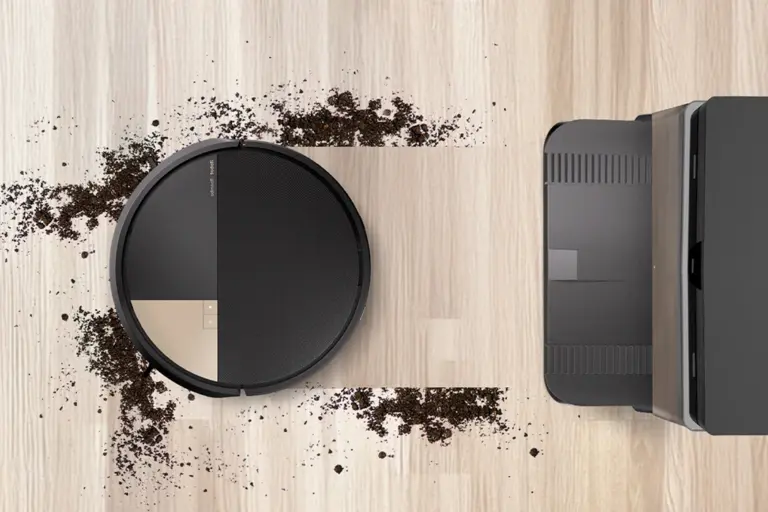 Robô aspirador iRobot visto de cima em piso de madeira, aspirando sujeira espalhada, com a base AutoWash ao lado
