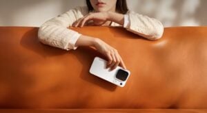 Mulher vestindo casado claro segurando o celular Find X10 Pro Max na cor Branco lunar enquanto se apoia em um sofá de couro marrom.