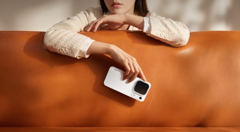 Mulher vestindo casado claro segurando o celular Find X10 Pro Max na cor Branco lunar enquanto se apoia em um sofá de couro marrom.